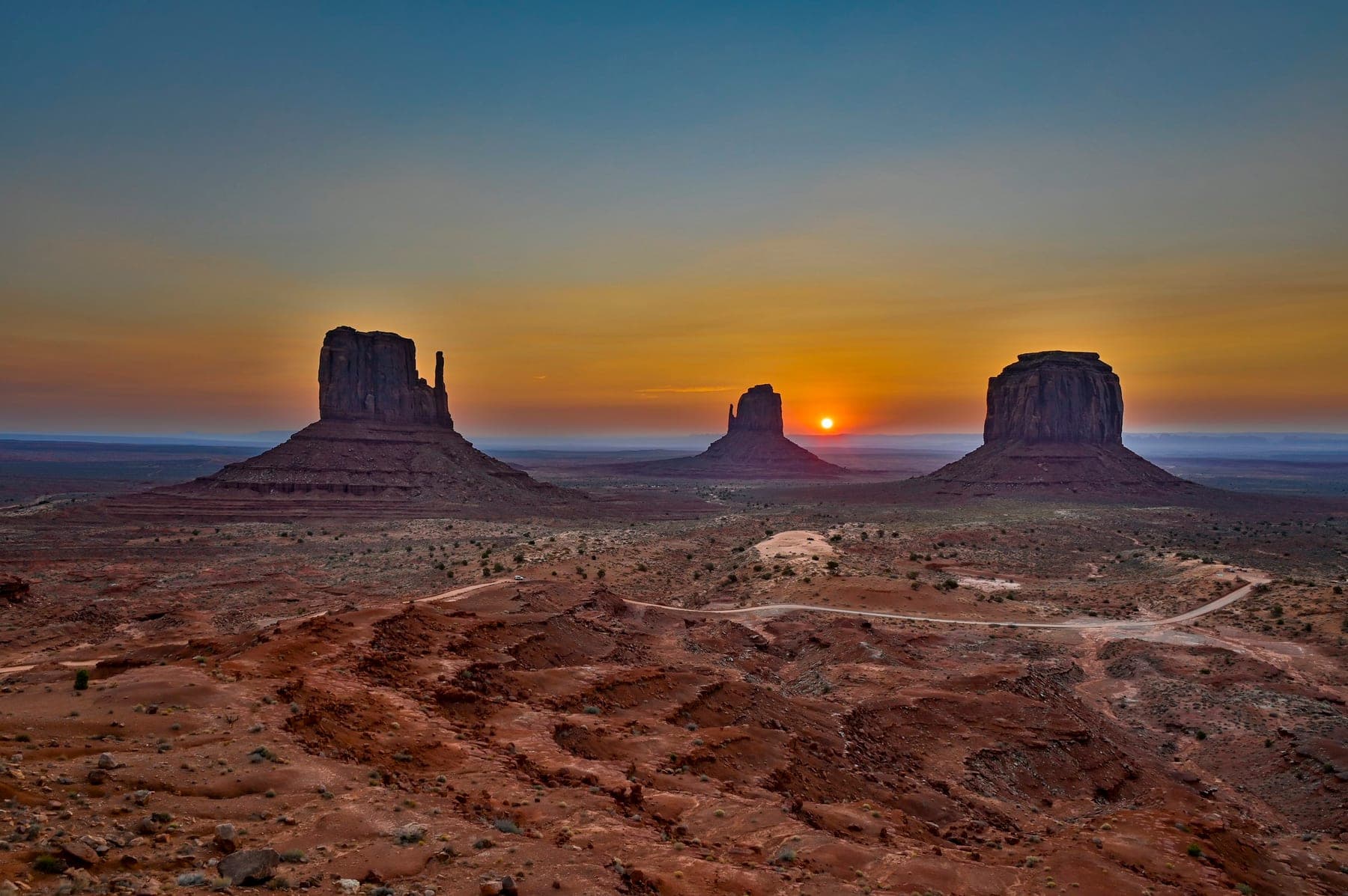 The Mittens buttes of Monument Valley silhouetted against a saturated sunset sky, a landscape by Carlton Soohoo