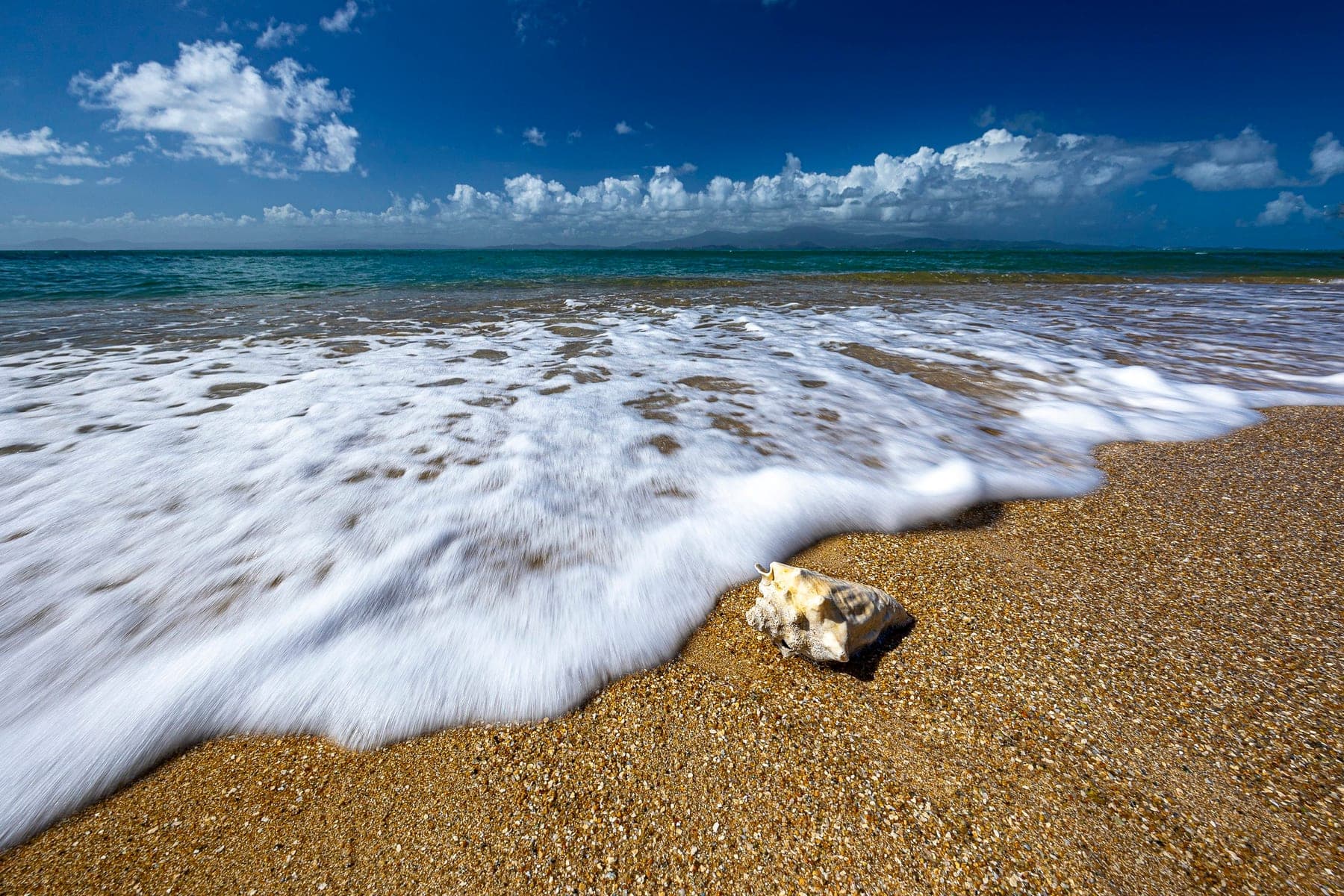 A breaking wave fanning across wet sand at the edge of the surf, long-exposure moving water