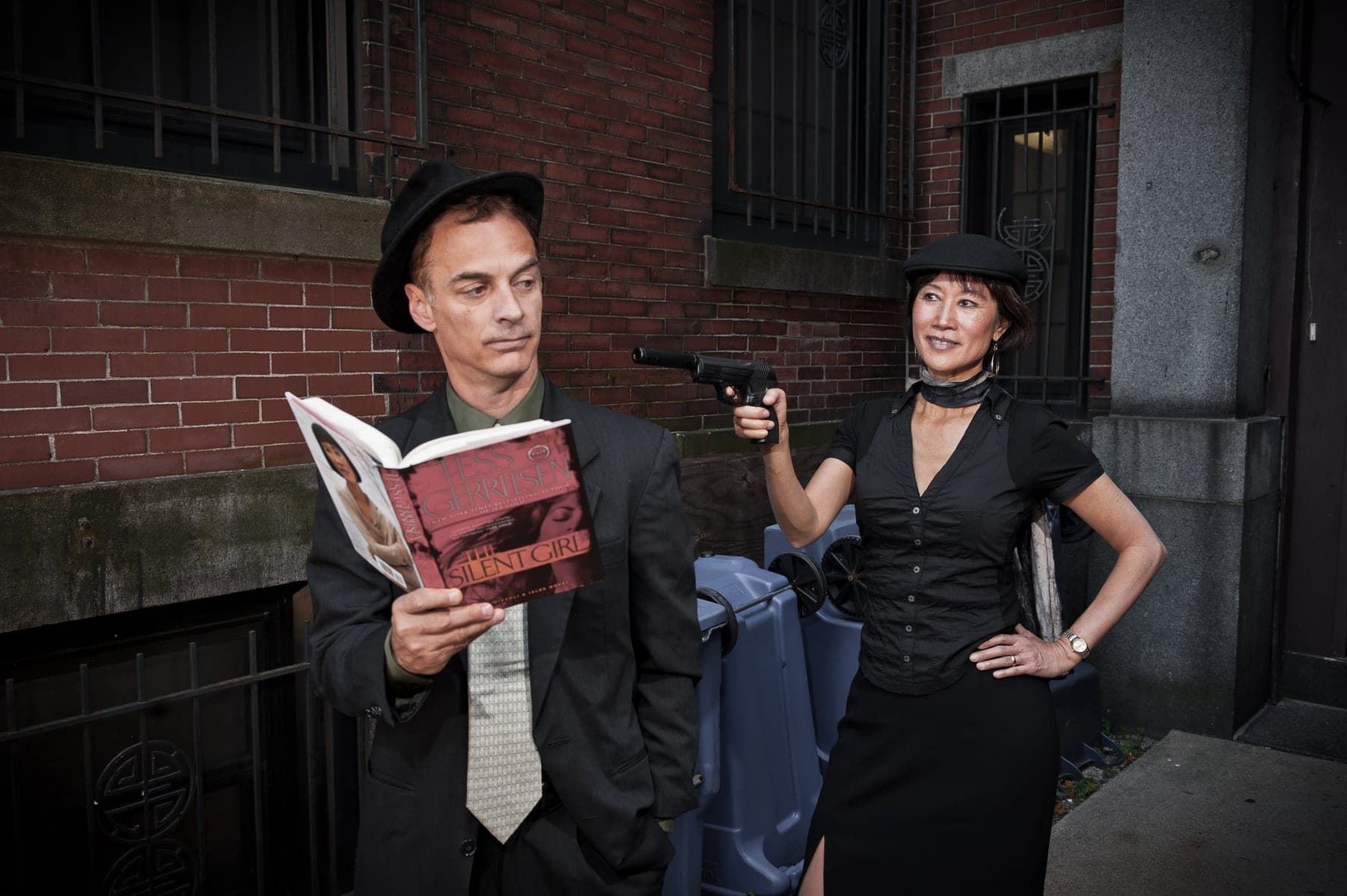 Two stylish figures in a moody alley, one reading, editorial fashion portrait